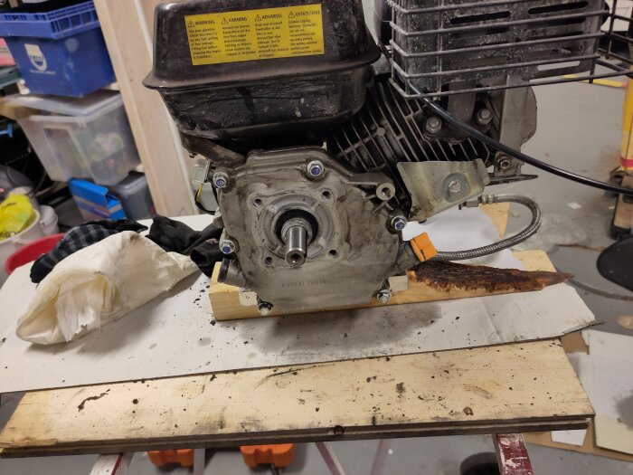 Motor på arbetsbänk under reparation, omgivet av verktyg och trasor i en verkstadsmiljö.