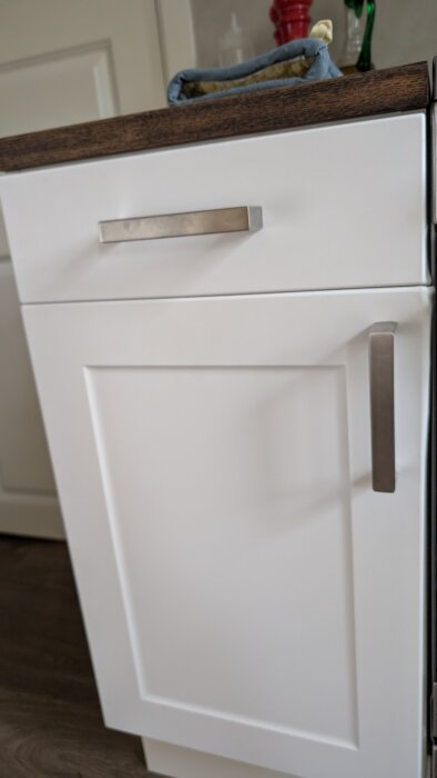 Vit kökslucka med metallhandtag, träbänkskiva ovanpå. Söker identifiering av märke för att matcha nyans och finish. Installerad 2018.