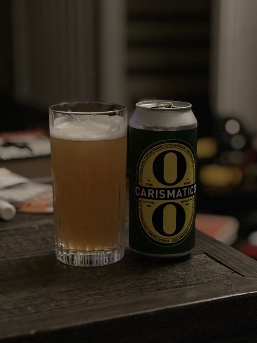 En glas fylld med öl bredvid en burk med etikett "Carismatico" på ett bord.