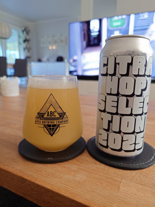 Glas med ljus öl från Apex Brewing Company bredvid en burk med texten "Citra Hop Selection 2023" på ett bord.