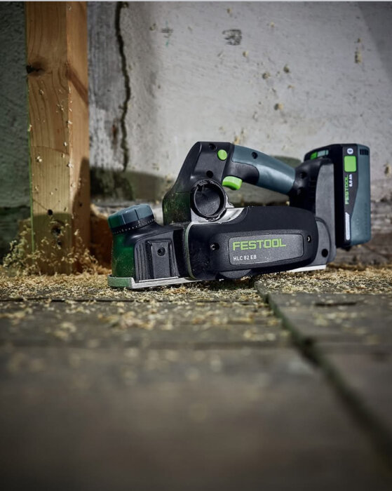 Elektriskt verktyg från Festool på ett golv, omgivet av sågspån och trä.