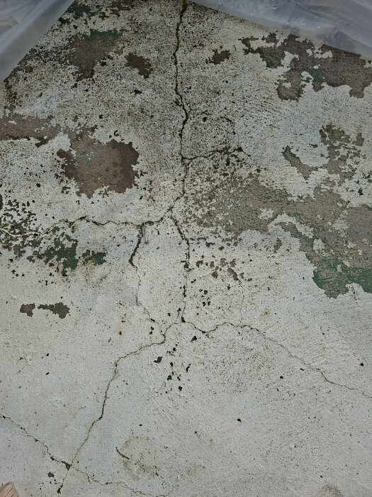 Sprucken betong på balkong med synliga sprickor och flagnande yta, som orsakar vattenläckage vid regn.