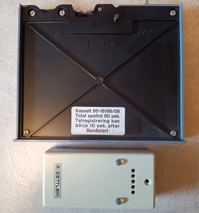 Zettler telefonsvarare med kassett och etikett om inspelningstid, samt tonsändare placerad på beige bakgrund.