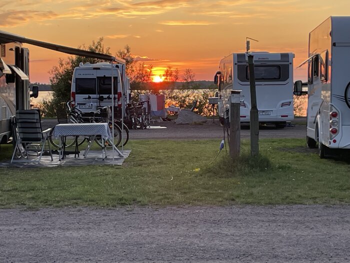 Solnedgång vid en camping i Vadstena med husbilar, cyklar och ett uppdukat bord i förgrunden.