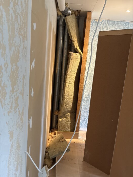 Ventilationsrör utan isolering synliga bakom borttagen garderob i renoveringsprojekt. Gammal isolering ligger på golvet.