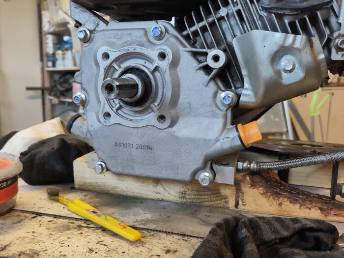 Motor med synlig avtappningsslang, verktyg och träblock i bakgrunden. Potentiell läcka diskuteras i samband med slangen.