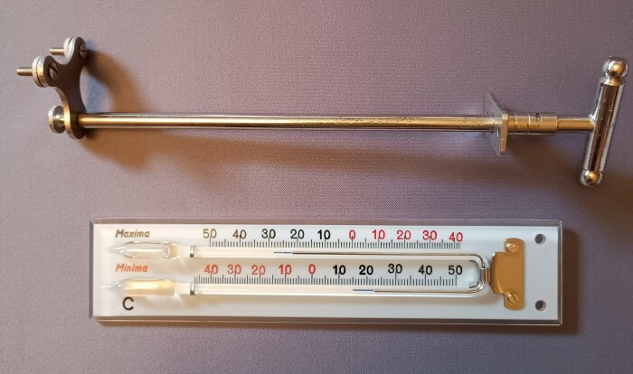 Max och minimumtermometer från Isidor Feingold med kvicksilverfyllt kapillärrör, gammal modell, metallgrepp och graderingar i Celsius.