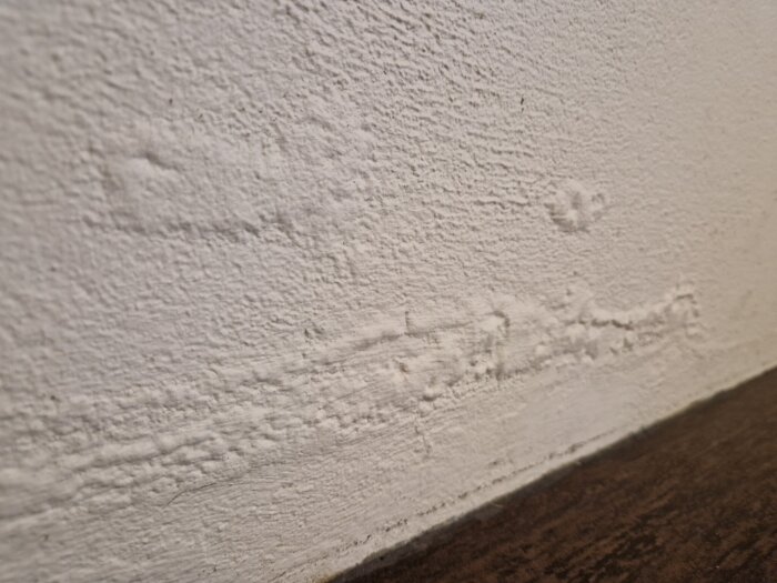 Bubblor på en målad innervägg ovanför golvet i ett 70-talshus.