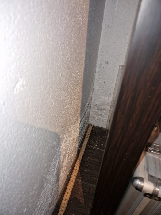 En vägg med vita bubblor i putsen nära golvet, med ett måttband längs väggen för skala.