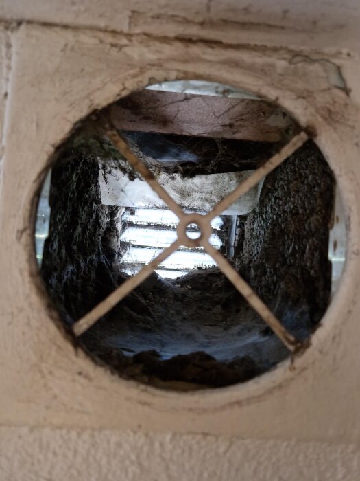 Smutsig ventilationskanal i källare med fyrkantiga hål i vägg, utan plaströr eller filter, visar på bristande luftflöde och behov av uppdatering.