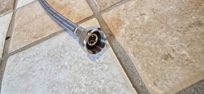 Metallomspunnen slang med R10-koppling liggande på ett kaklat golv, del av installation av en ny blandare.