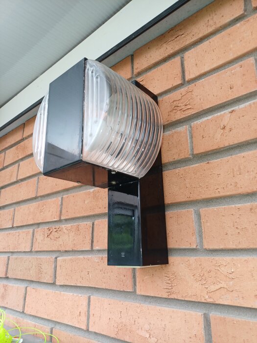 Vägglampa monterad på tegelfasad, utan synligt eluttag, med fokus på lampans design och material.