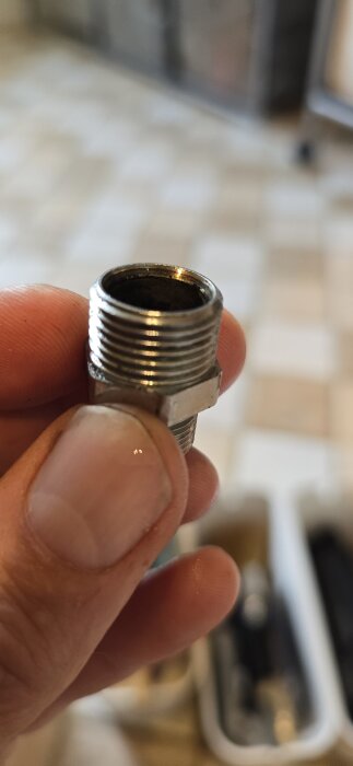 Närbild av en övergångsnippel i metall som hålls mellan fingrarna, med gängor synliga på båda sidor.