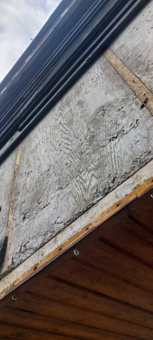 Betongvägg med ingjuten spikläkt synlig bakom avlägsnad fasadpanel, del av byggnadsprojekt.