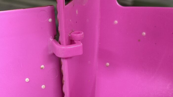 Närbild av ett rosa plastgångjärn och detaljer av en sprucken leksaksdel från ett loppisfynd, med synliga popnitar.