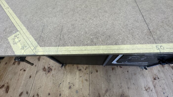 En träskiva med markerad oktagonal form och gradtal skrivet på tejpen, placerad på ett plankgolv i verkstadsmiljö.