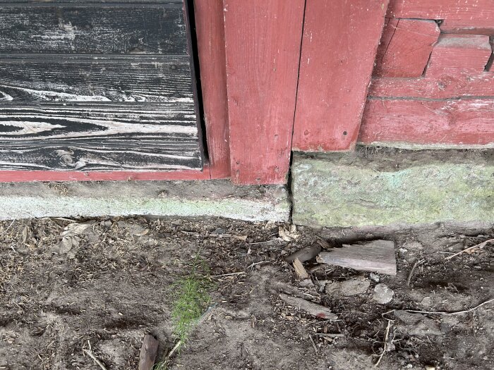 Närbild på grunden av en timmerlada med två olika material: en betonggrund och en stengrund, samt träpanel ovanpå.