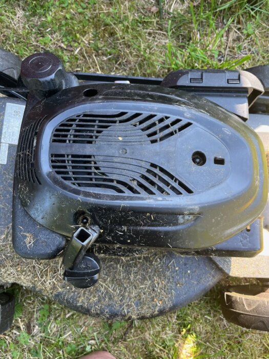 Bild av motoröverdraget på en Stiga Combi 553 S gräsklippare, med startenheten synlig längst fram. Gräset syns runtomkring.