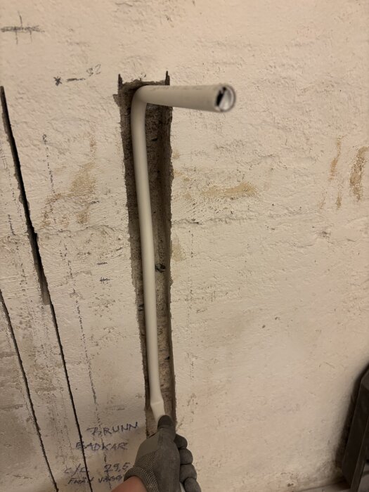 Vitt plaströr monteras i en urholkning i väggen för duschinstallation, handskbeklädd hand håller i röret.