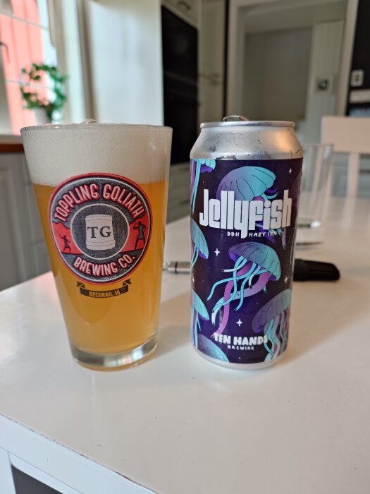 Ölglas från Toppling Goliath och burk Jellyfish DDH Hazy IPA från Ten Hands på ett bord.