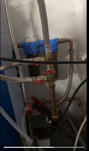VVS-installation i källare med kopparrör, filter och ventiler; eventuellt en pump vid basen.