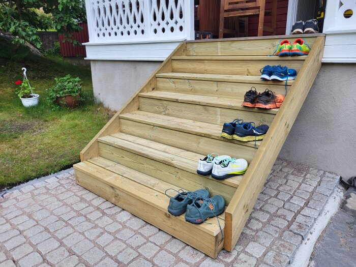En nybyggd trätrappa utanför hus med flera par skor på stegen, trädgård i bakgrunden.