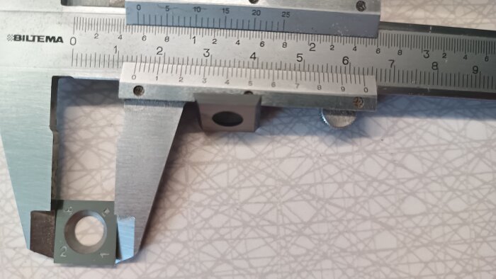 Närbild på en skjutmått med Biltema-märke som mäter ett metallföremål på en mönstrad yta.