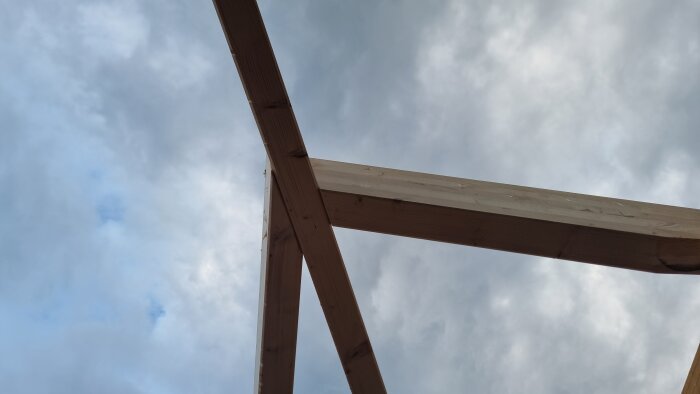 Träkonstruktion i z-formad struktur mot molnig himmel efter regn, en del av ett byggprojekt med inslag av sekelskifte och modern stil.