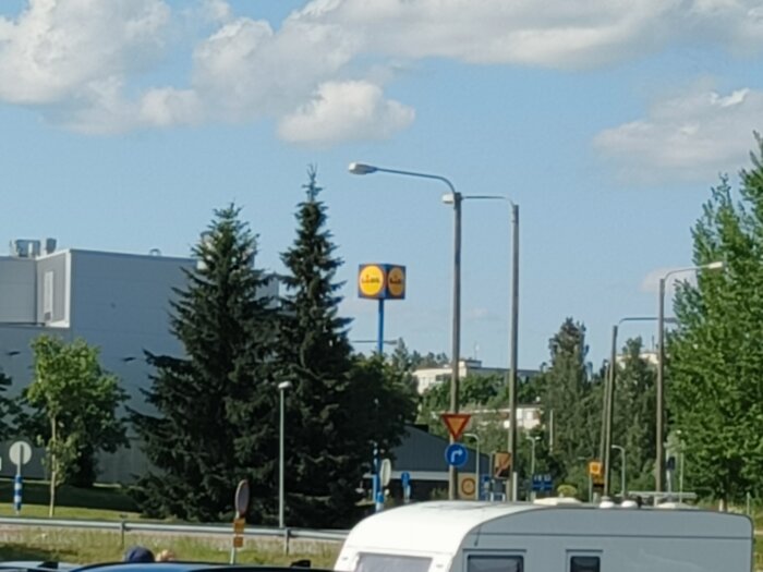 Skylt för Lidl synlig bakom flera träd och stolpar på en solig dag.