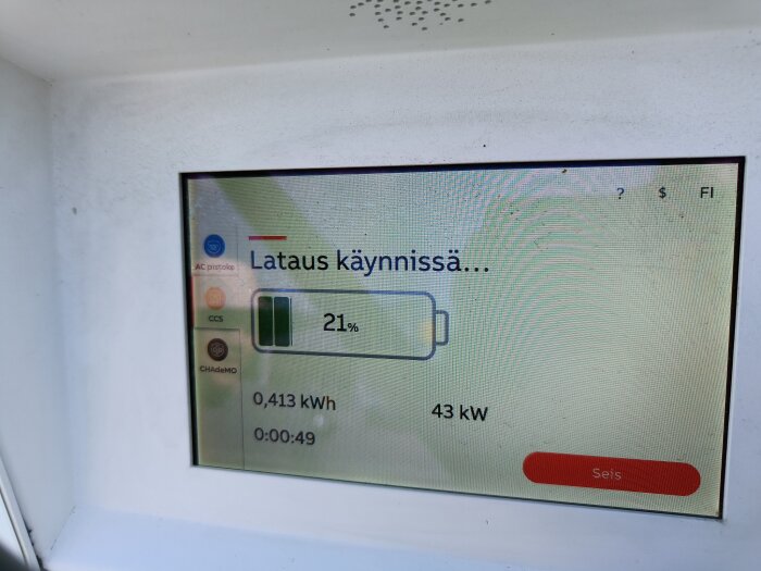 Laddningsstationens skärm visar 21% batteri, 0,413 kWh förbrukat, 43 kW effekt och en laddningstid på 49 sekunder. Text på finska: "Lataus käynnissä".