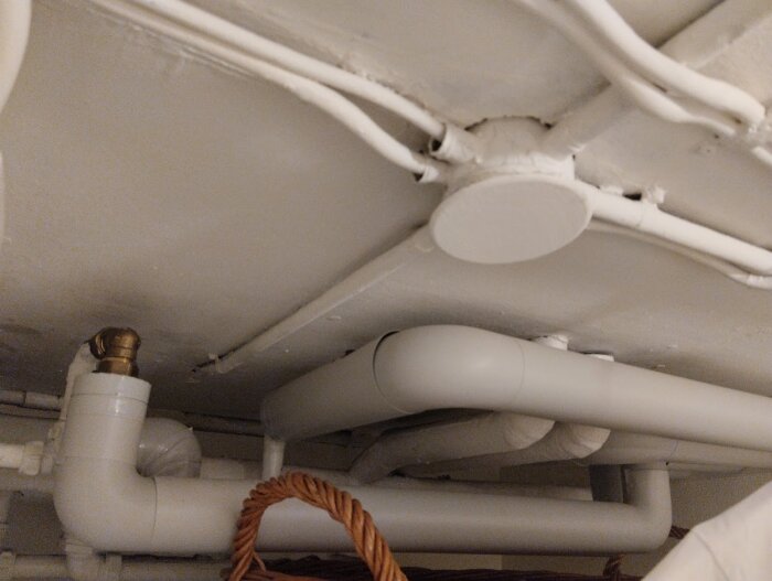 Eternitplattor med elinstallationer och vattenrör i ett källartak, potentiellt med asbest.