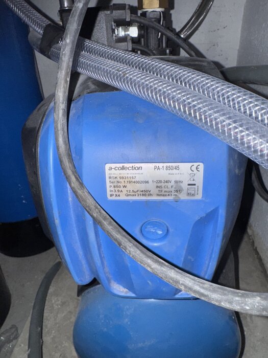 Blå vattenpump med etikett "a-collection" och modell PA-1 850/45, omgiven av slangar och kablar. Pumpen har slutat fungera.