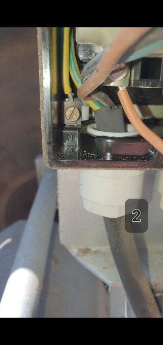 Kabeldragning i strömbrytare med gul/grön jordkabel kopplad tillsammans med orange kabel, märkt med "N", del av vedklyv.