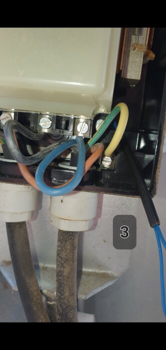 Kabelinstallation i en elströmbrytare; gul och grön jordkabel ansluten till nolluttaget till höger, andra kablar kopplade till olika skruvterminaler.