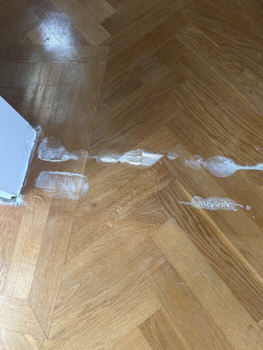 Parkettgolv med limrester efter nedtagning av vägg, synliga som vita fläckar längs betongväggens tidigare placering.