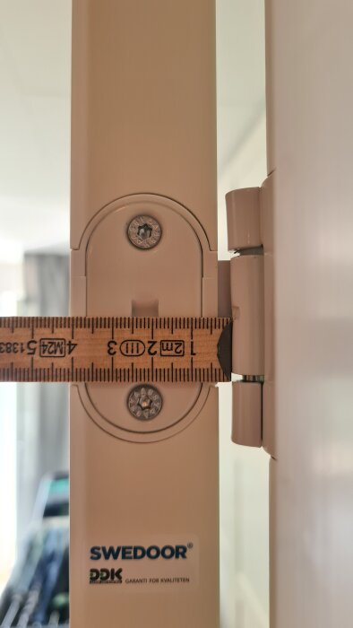 Närbild av dörrgångjärn med linjal som mäter avståndet mellan dörr och karm, ca 2-3mm, med text "Swedoor" synlig på karmen.