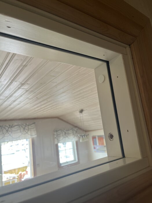 Väggmonterat glasfönster i en lägenhet från 80-talet, fäst med spikpistol, utan synliga skruvar för demontering.