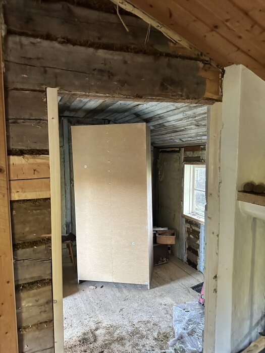 En delvis riven timmervägg i en renoverad stuga, där en ny dörröppning syns. Panelen ska ersättas av OSB, och förstärkning behövs.