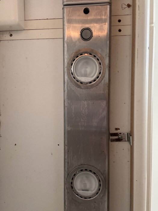 Ljusramp i metall monterad under köksskåp med två runda inbyggda lampor och en knapp ovanpå.