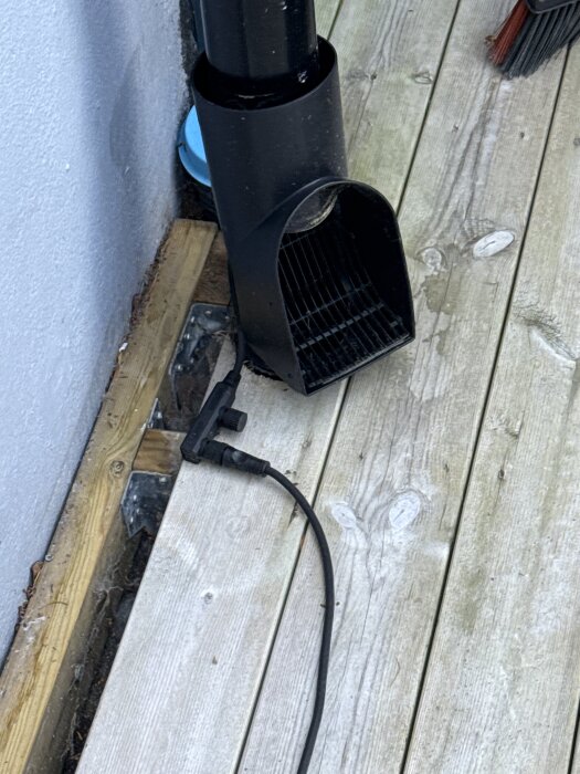 Svart flexrör och elledning vid sidan av husvägg under trädäck.