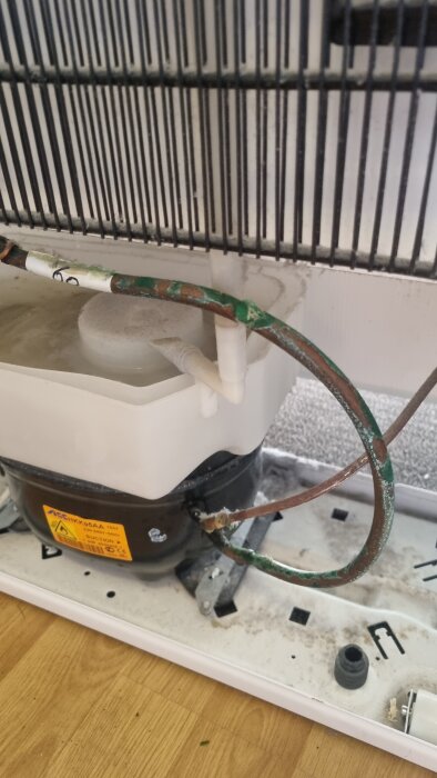 Kylsystem med missfärgade rör nära kompressor, potentiell kylmedieläckage eller kondensindikering.