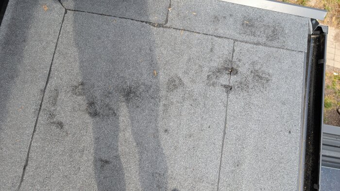 Ny ytpapp på balkong med märken eller skador på ytan, delvis i skugga, med plåtkanter runt om och några små pinnar ovanpå.