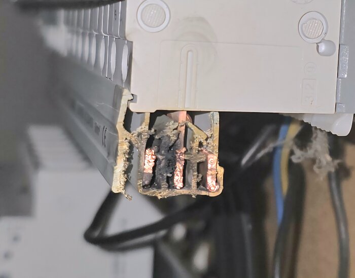 Bränd och skadad kopplingslist med exponerade kopparledare i en elcentral, potentiellt orsakat av elfel eller dålig installation.