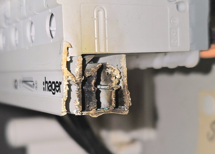 Närbild av skadad elcentral med bränd och deformerad fasskena, märkt "Hager", i bastu med elfel.