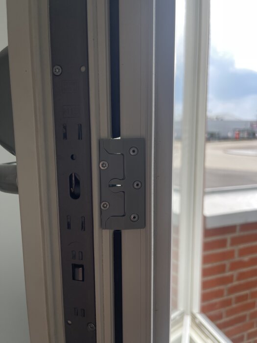 Fönsterkarm med låsdetalj, oöppnade glasrutor och utsikt över tegelvägg.