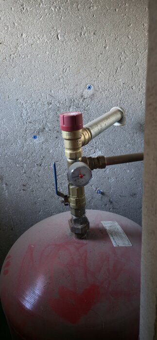 Tryckmätare på ett expansionskärl i pannrummet. Mätaren visar trycket i systemet och har två pekare. En påfyllningsventil syns också.