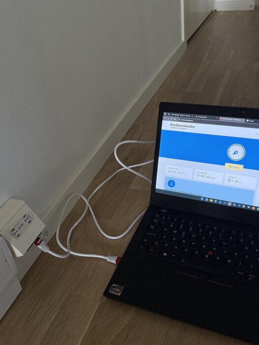 Laptop ansluten till väggmonterat nätverksuttag med platt nätverkskabel, bredbandskollen visas på skärmen.