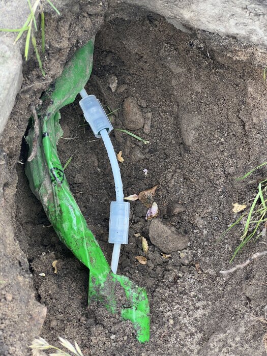 Grön fiberoptisk kabel och skarvkoppling synliga i en uppgrävd jordgrop. Fiberledningen har nyligen reparerats.