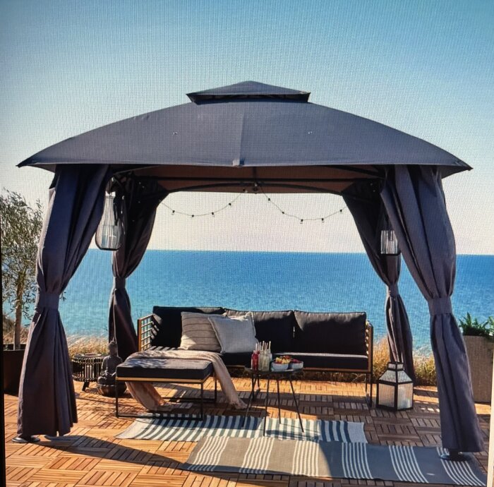 Paviljong med mörka gardiner, soffa, och bord med havsutsikt.