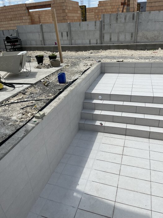 En nyligen kaklad trappa och golv vid byggarbetsplats, med omgivande rå betongväggar och byggmaterial i bakgrunden.